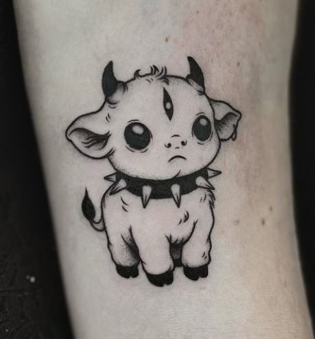 a small black and white animal tattoo on the ankle with an adorable little baby cow