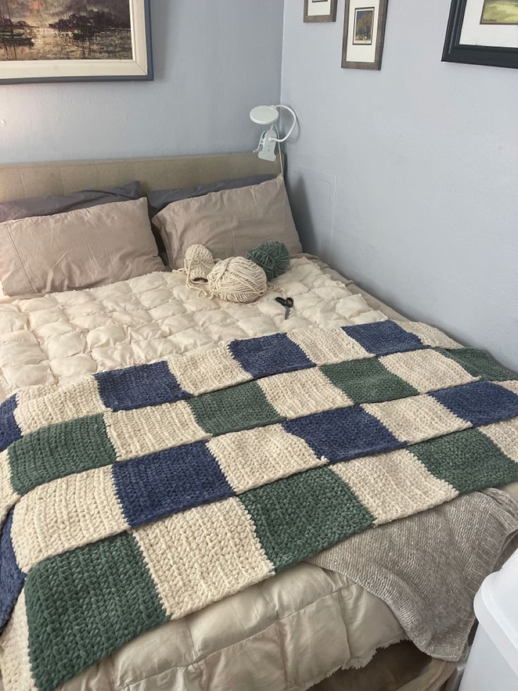 a bed with a blanket and pillows on top of it in a bedroom next to two framed pictures