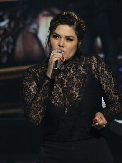 a woman holding a microphone in her right hand and wearing a black lace top on stage