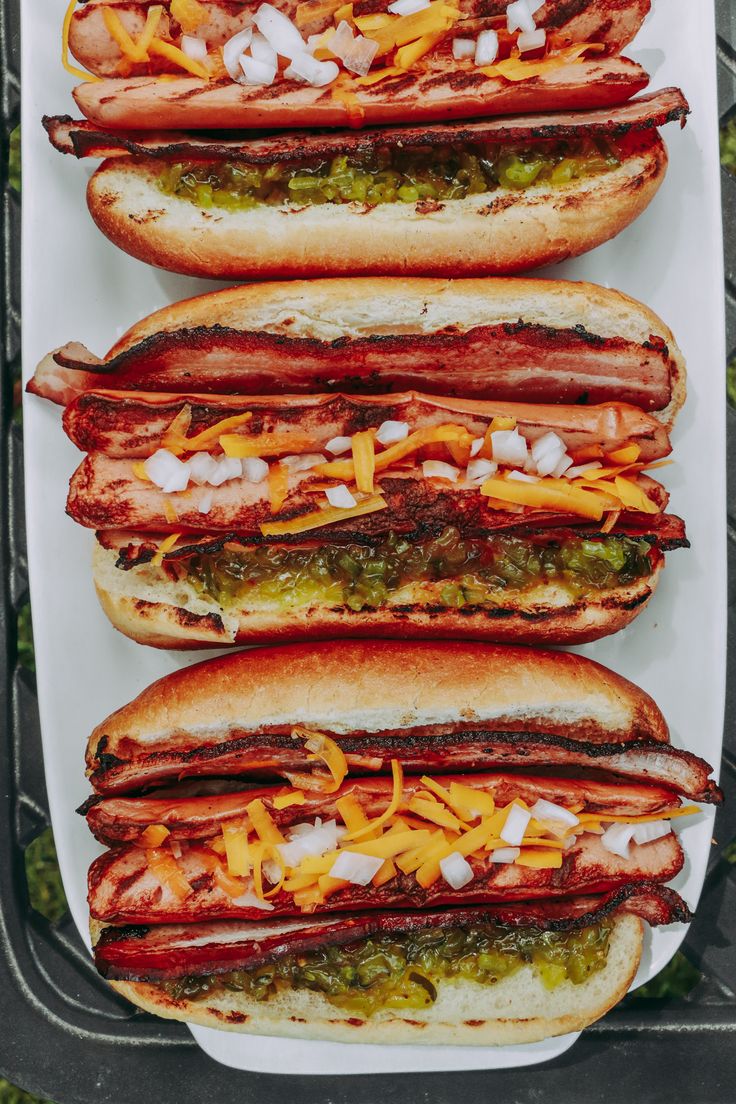 three hot dogs with cheese and relish in buns on a tray outdoors, ready to be eaten