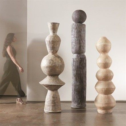 a woman walking past three tall vases in an art gallery, each with different shapes and sizes