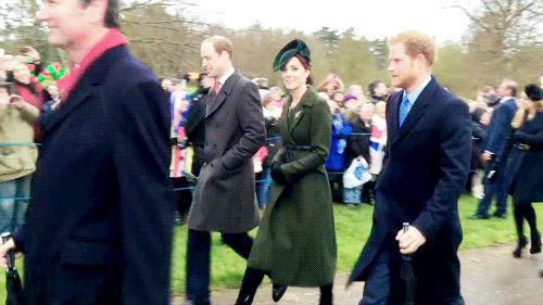 the prince and princess are walking together in front of a large group of people wearing coats