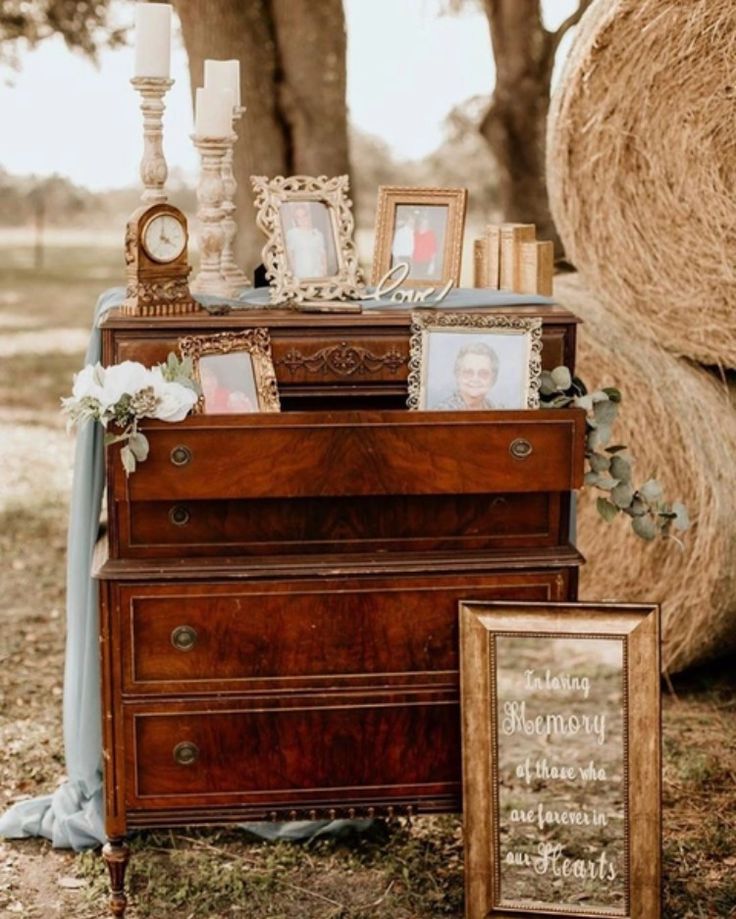 an old dresser with pictures and candles on it next to a hay bale in the background