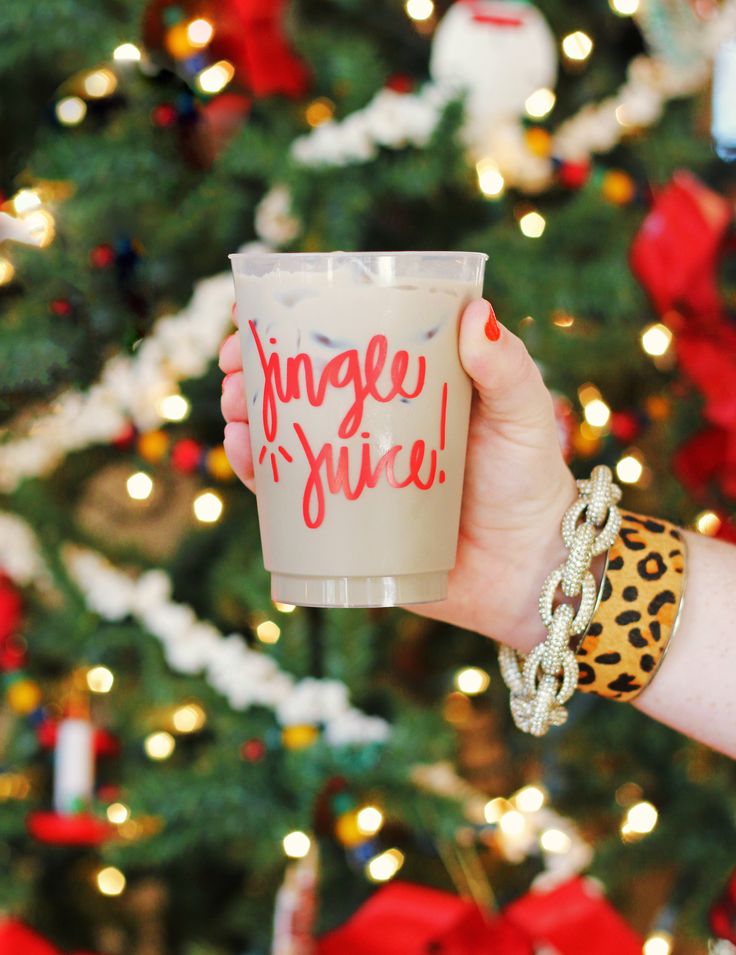 a woman holding up a coffee cup in front of a christmas tree