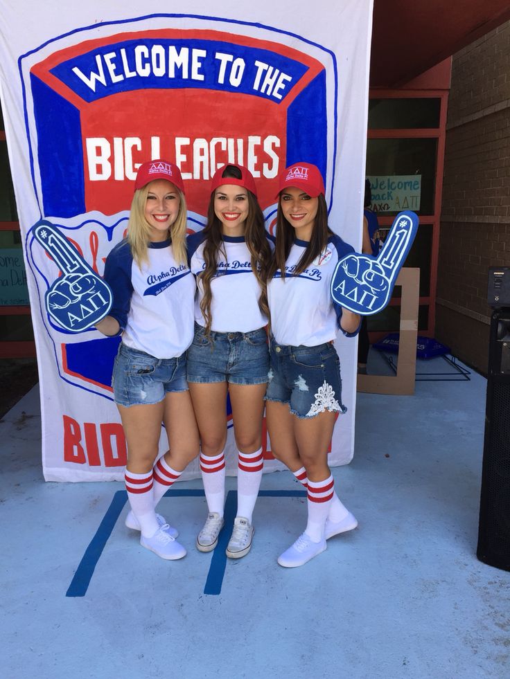 three girls are posing in front of a big league banner