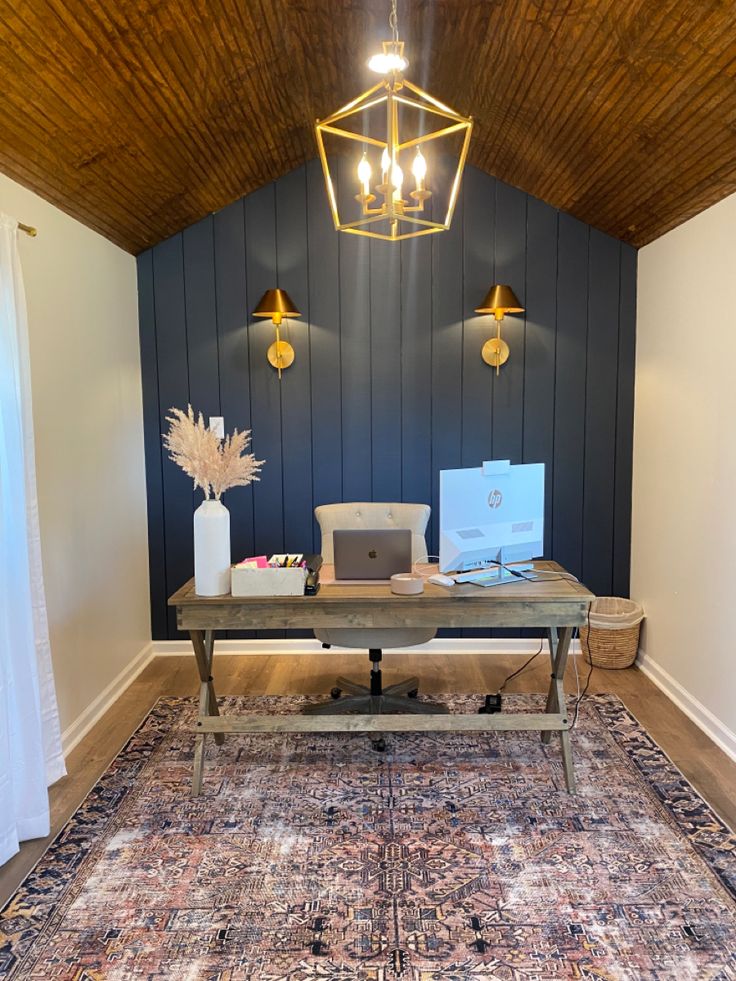 a desk with a laptop on top of it in front of a blue wall and wooden ceiling