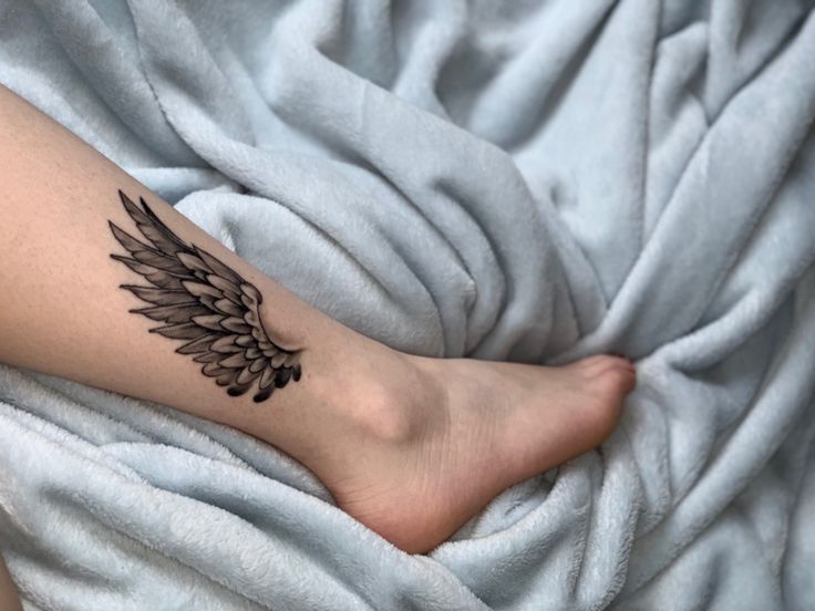 a woman's foot with a tattoo on it and an angel wing in the middle