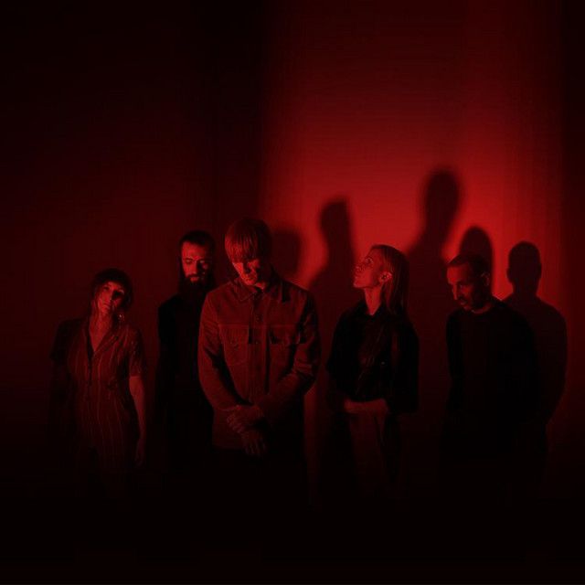 a group of people standing in front of a red wall with their shadows on the wall