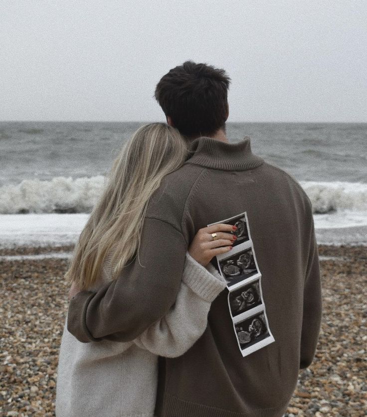 a man and woman standing next to each other on a beach with the ocean in the background