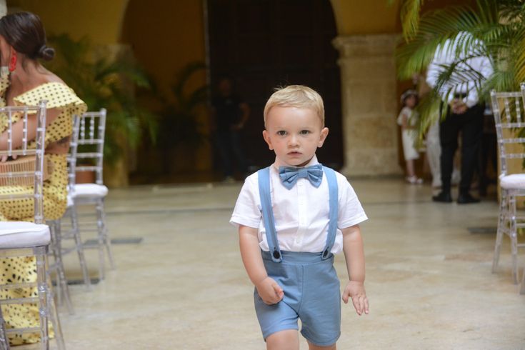 a little boy in blue shorts and bow tie walking down the aisle at a wedding