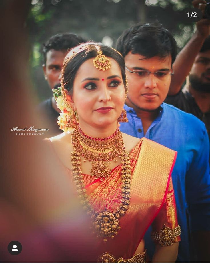 a woman in a yellow sari and necklace standing next to another man wearing a blue shirt