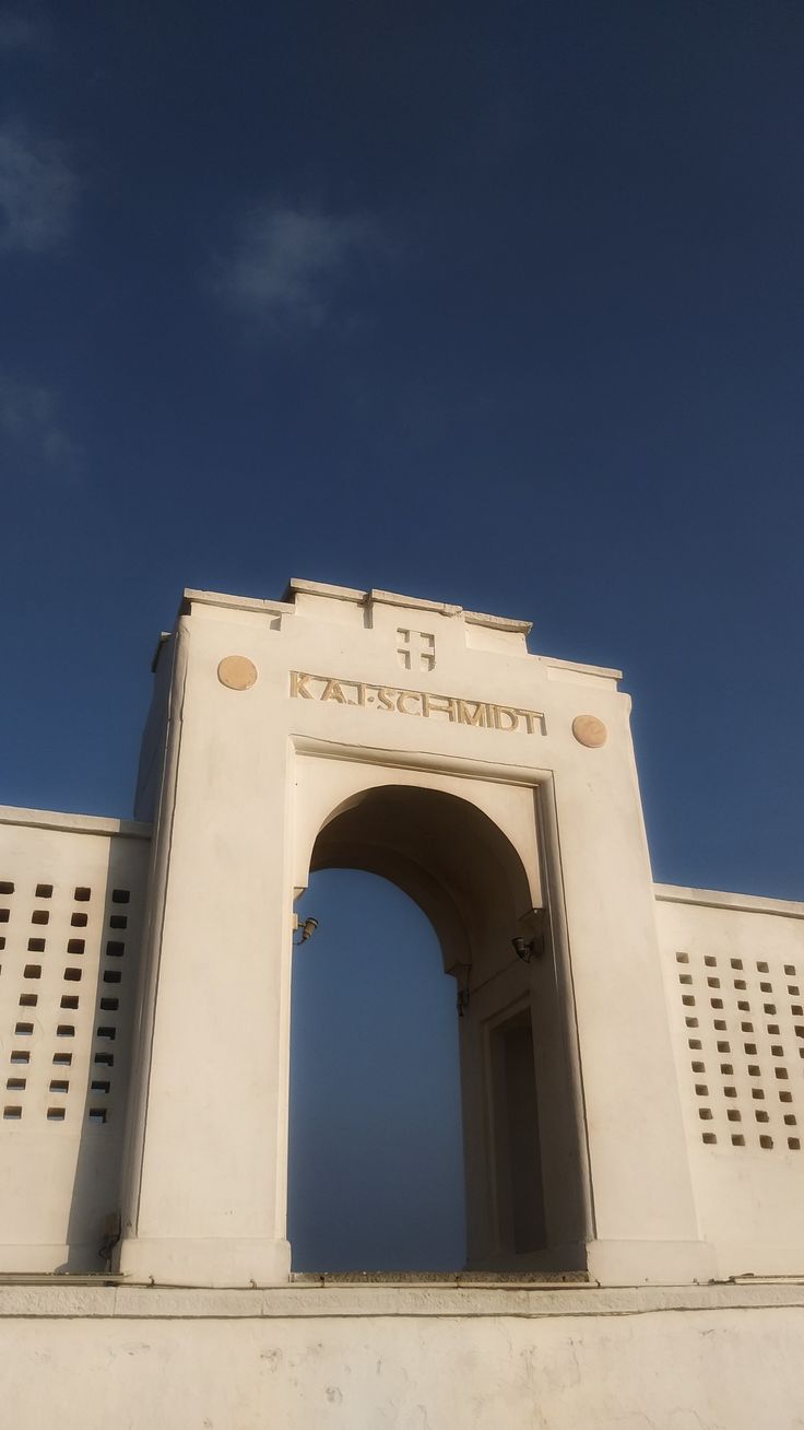 the entrance to an old white building with a clock on it's side and blue sky in the background