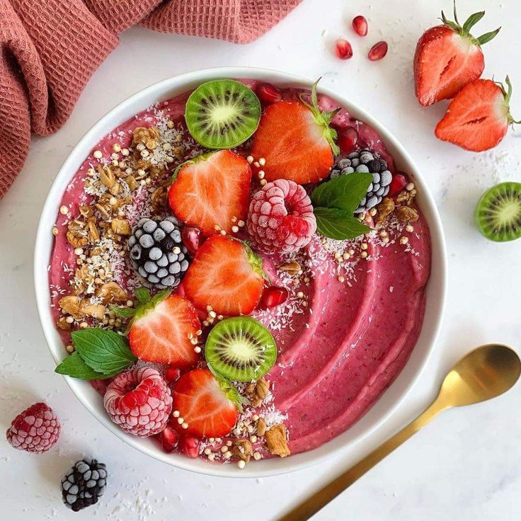 a bowl filled with berries, kiwis and granola on top of a white table