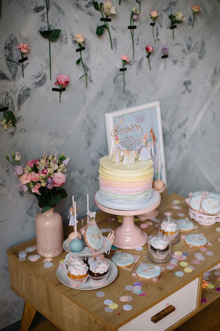 a table topped with cake and cupcakes next to a wall covered in flowers