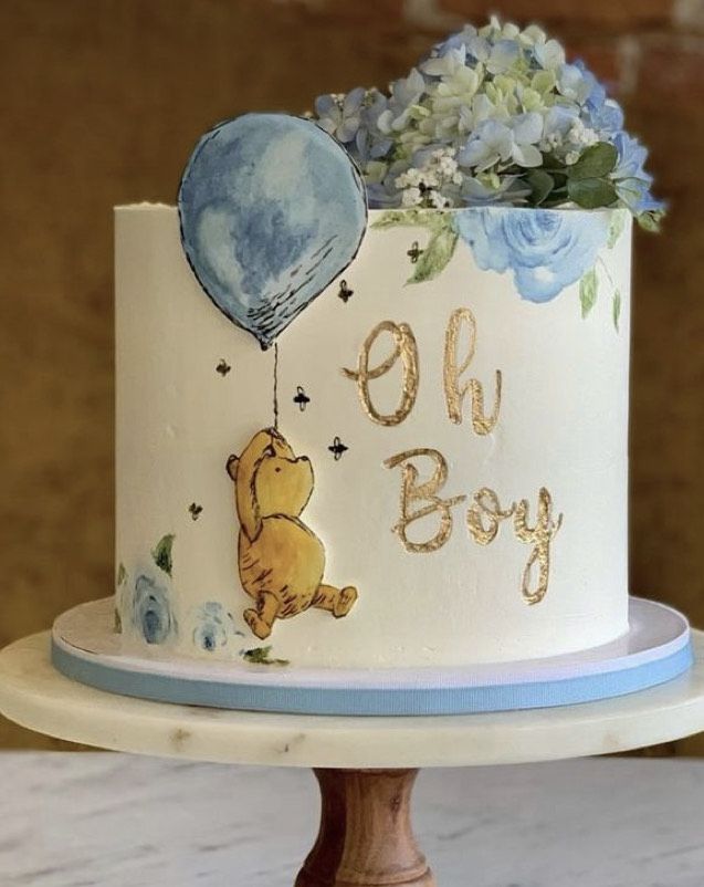 a winnie the pooh birthday cake with blue flowers and balloons is on a wooden stand