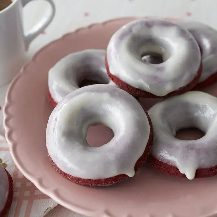 three donuts with white icing on a pink plate next to a cup of coffee