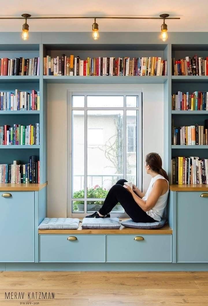 a woman sitting on a window sill in front of a book shelf filled with books