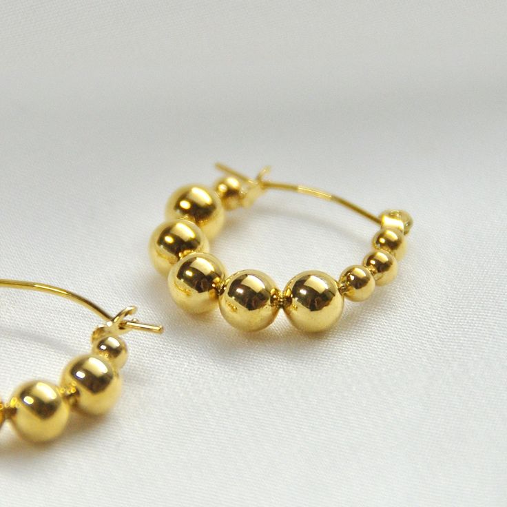 Beaded Hoop Earrings14K Gold Plated Stainless SteelOur Beaded Hoops are the perfect marriage of elegance and charm and will make a delightful addition to any jewelry collection. This lightweight accessory is minimalist in make, yet timeless in style. The unique pair is made with 14K Gold Plated Stainless Steel allowing its color to remain over time.All of our products are lightweight and made with hypoallergenic materials to allow for comfortable, all day wear.The Beaded Hoop Earrings are the pe Yellow Gold Beaded Hoop Earrings For Gift, Gold Hoop Earrings With Round Beads, Gold 14k Gold-filled Hoop Earrings With Round Beads, Gold Earrings With Polished Beads For Wedding, Gold Round Beads Earrings For Everyday, Everyday Gold Round Bead Earrings, Everyday Gold Beaded Round Earrings, Elegant Hoop Earrings With Gold Beads, Everyday Gold Beaded Earrings