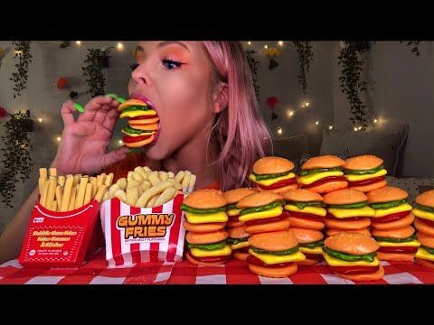 a woman eating hamburgers and french fries in front of a table full of food