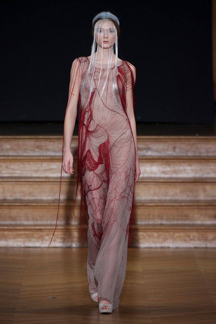 a model walks down the runway in a sheer red dress with long veils on her head