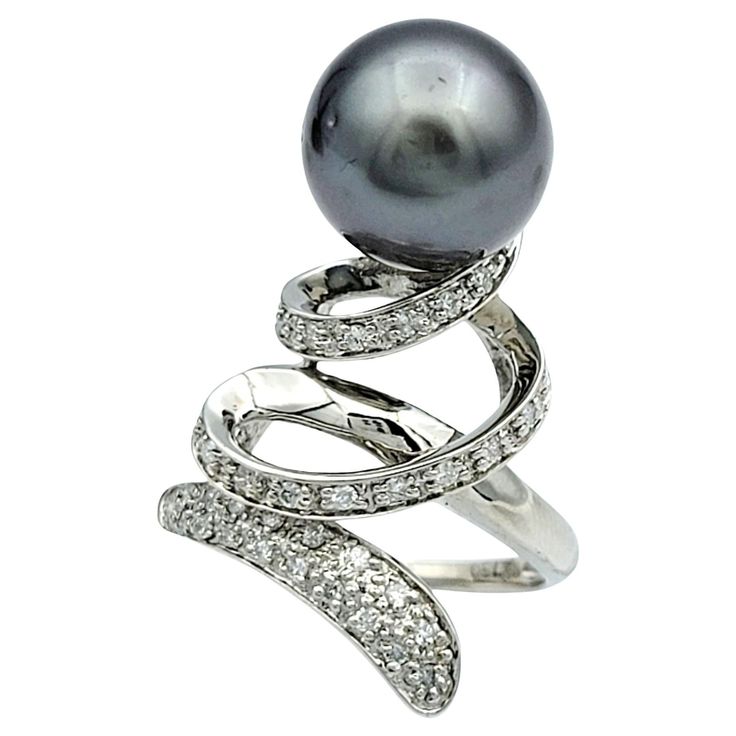 Ring Size: 7 This captivating black pearl and diamond cocktail ring boasts a mesmerizing spiral design and set in luxurious 18 karat white gold. At its heart lies a lustrous black pearl, exuding an aura of mystery and sophistication. Paired with the pearl, a dazzling array of diamonds trace a graceful spiral, accentuating its beauty with every curve. This exquisite ring is a testament to refined craftsmanship and timeless elegance, perfect for making a statement at any event. This piece is in very good estate condition and has been professionally cleaned and polished. Metal: 18 Karat White Gold Gemstones: Black Pearl and Diamonds Pearl Count: 1 Pearl Shape: Round Pearl Color: Black Diamond Cut: Round Diamond Total Carat Weight: 0.20 carats Diamond Color: H - I Diamond Clarity: SI2 Ring Wei Trace A, Diamond Cocktail Ring, Diamond Cocktail Rings, Spiral Design, Pearl Diamond, Pearl Color, Black Pearl, Ring Size 7, Cocktail Ring