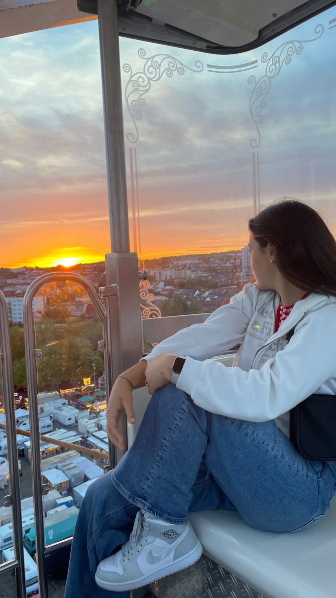 a woman sitting on top of a building looking out at the sun setting behind her