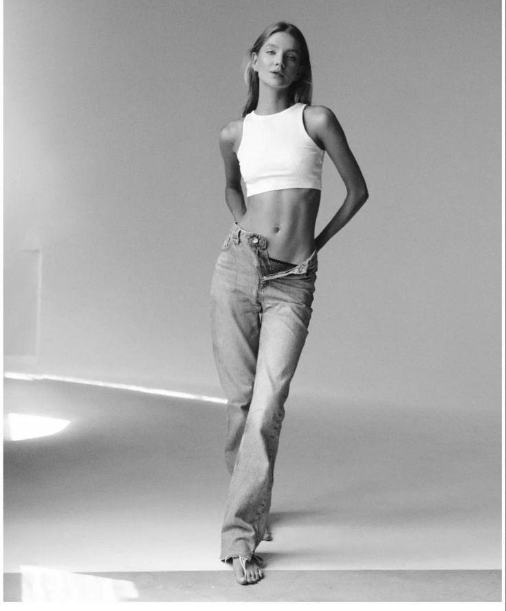 a black and white photo of a woman in high waist jeans with her hands on her hips