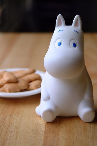 a white cat figurine sitting on top of a wooden table next to a plate of cookies