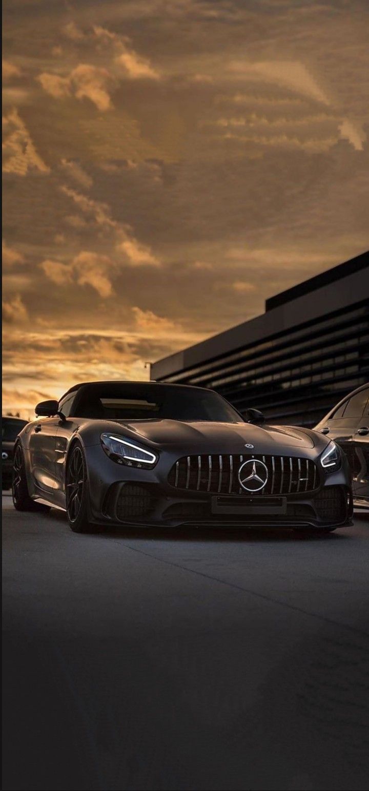 two mercedess are parked in front of a building at sunset with the sun behind them