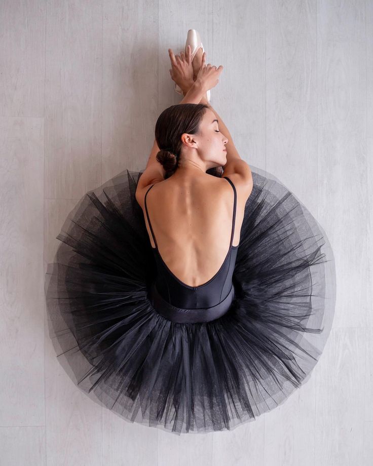 a woman in a black tutu is reaching up to catch a white ball with her hands