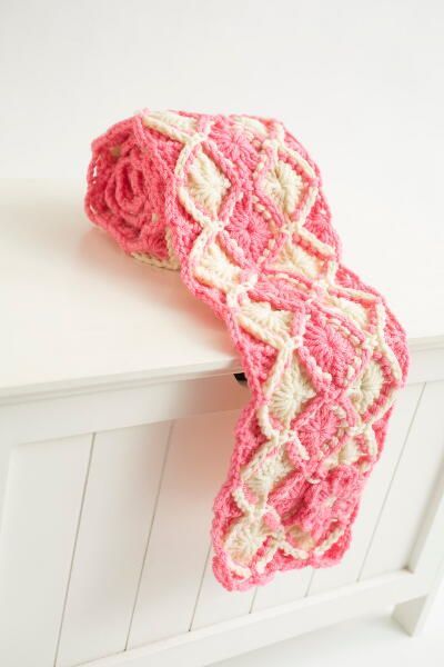 a crocheted pink and white scarf hanging from a door handle on a cabinet