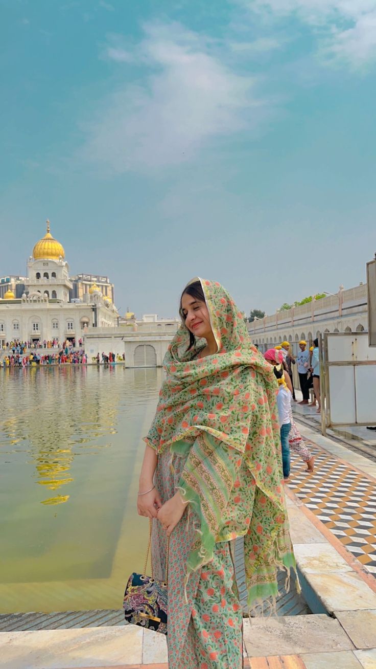 a woman standing in front of a body of water wearing a green and yellow shawl