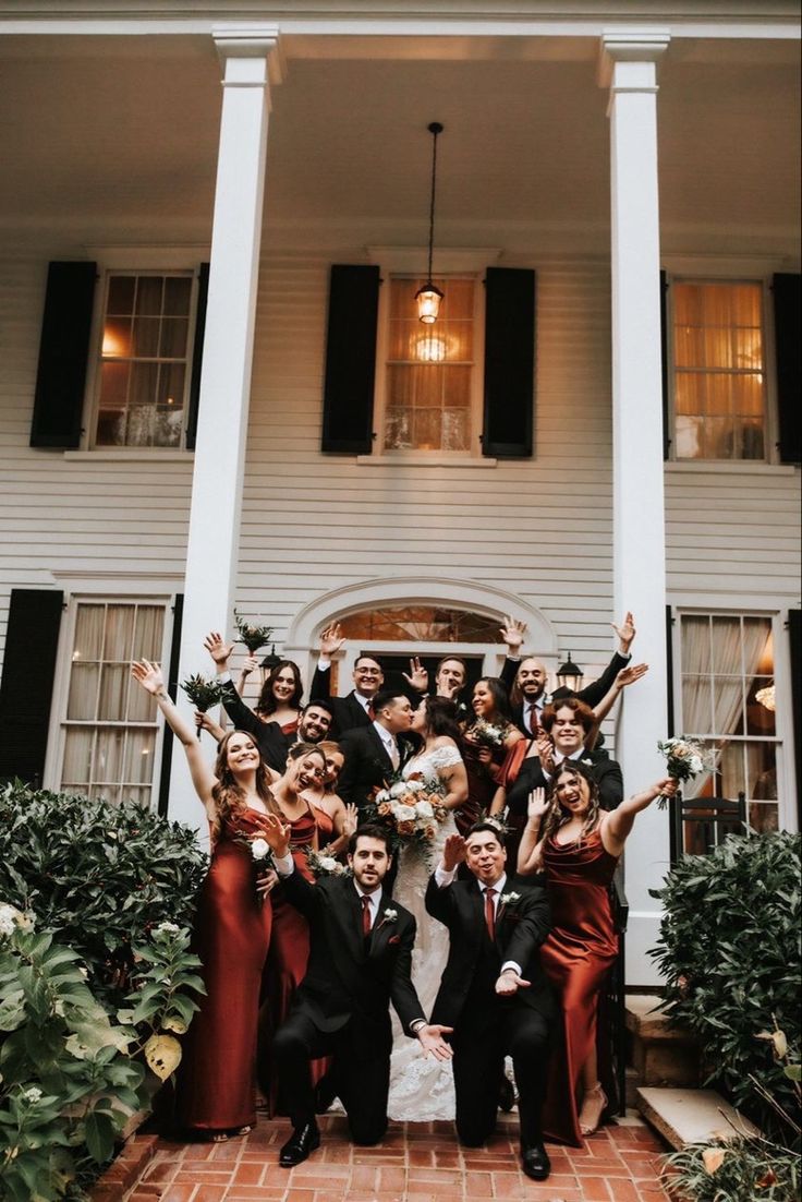 a group of people standing in front of a white house with their arms up and hands out