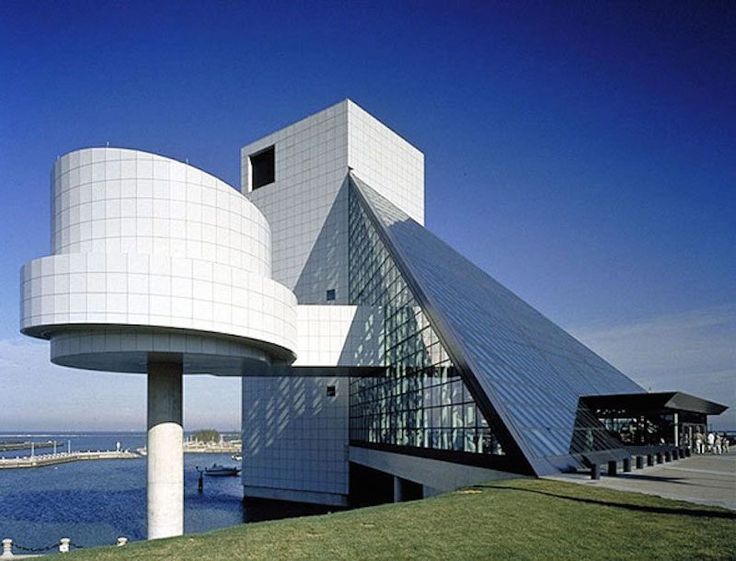 an unusual building sits on the edge of a body of water with grass in front of it