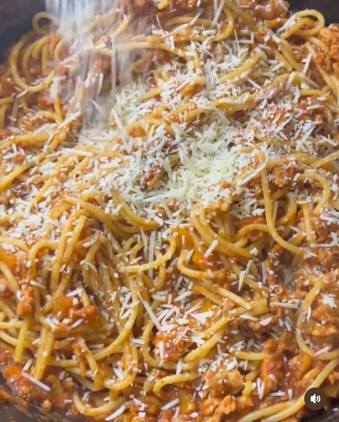 pasta being cooked in a skillet with parmesan cheese and sauce on top