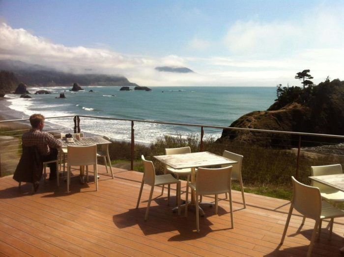 a person sitting at an outdoor table on a deck overlooking the ocean and cliffs in the distance