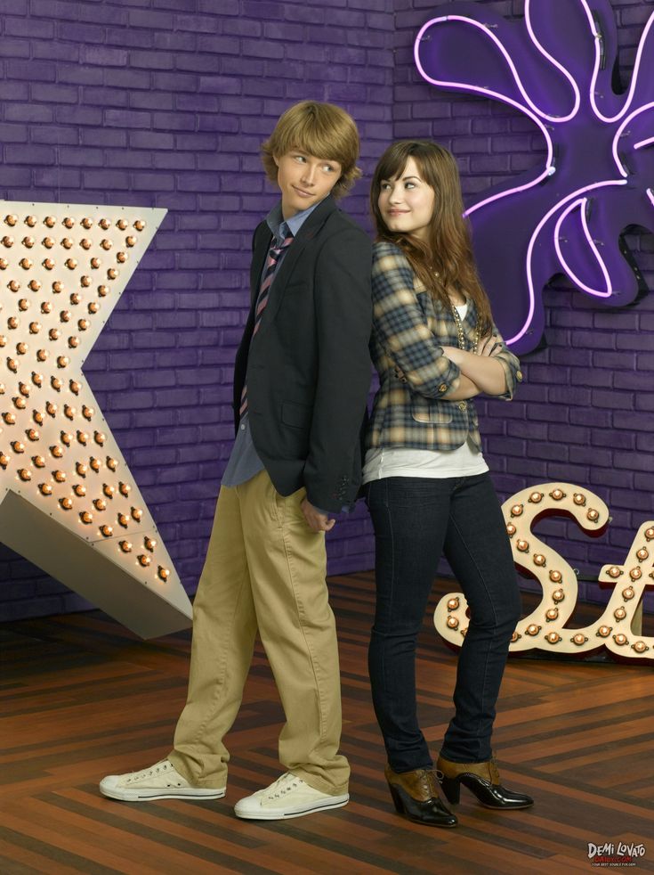 two people standing next to each other in front of a purple brick wall with the word sale on it