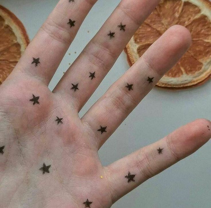 a person's hand with tiny black stars on it and orange slices in the background