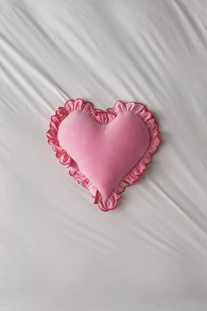 a pink heart shaped pillow sitting on top of a bed