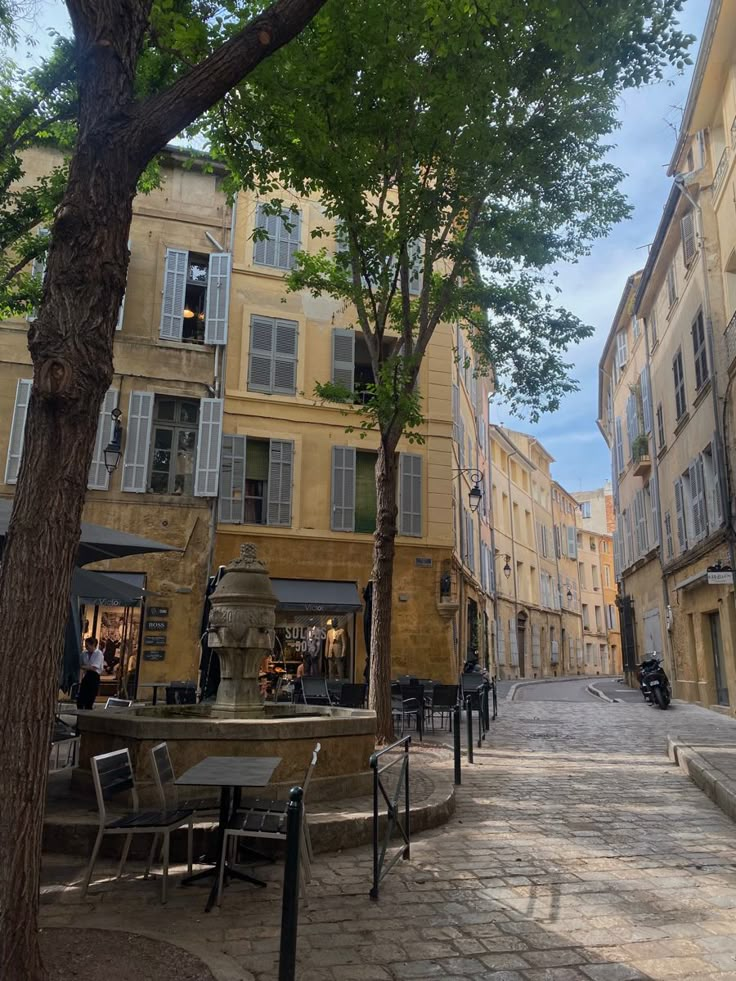 an empty city street with tables and chairs on the side walk next to tall buildings