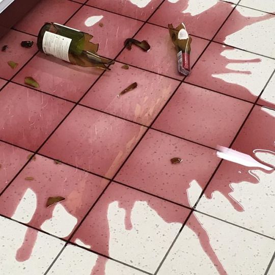 a wine bottle that is sitting on the ground with spilled paint all over it's surface