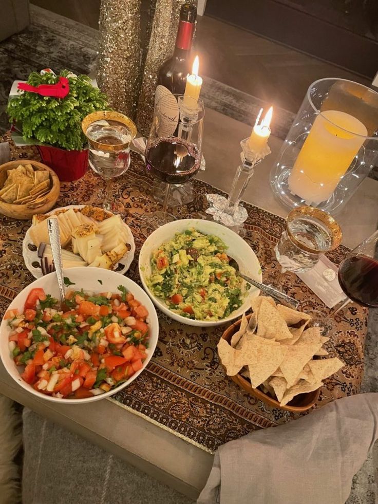 a table topped with bowls of food next to glasses of wine and plates of chips