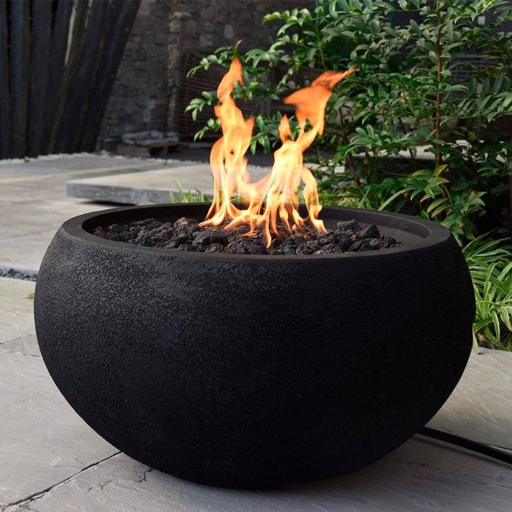 an outdoor fire pit sitting on top of a cement floor next to trees and bushes