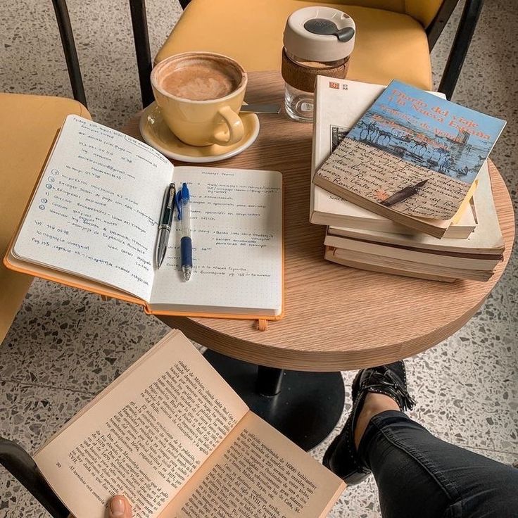 a person sitting at a table with several books and a cup of coffee on it