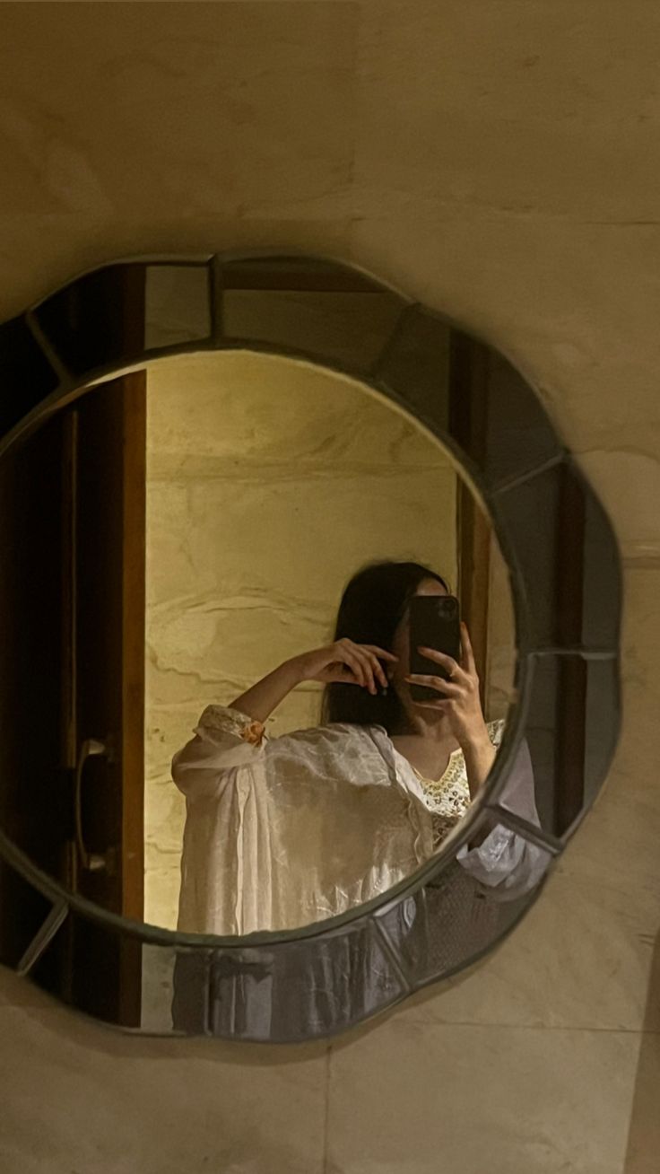 a woman taking a selfie with her cell phone in front of a round mirror