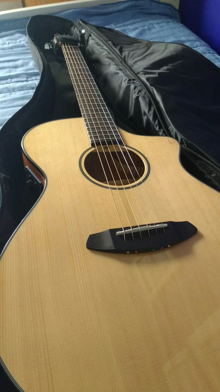 an acoustic guitar laying on top of a bed next to a black case and pillow