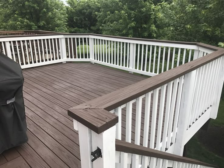 a deck with white railings and an outdoor grill cover on the top, surrounded by trees