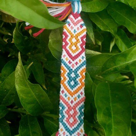 a colorful beaded tie hanging from a tree branch with leaves in the foreground