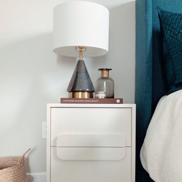 a nightstand with a lamp on top of it next to a blue headboard and bed