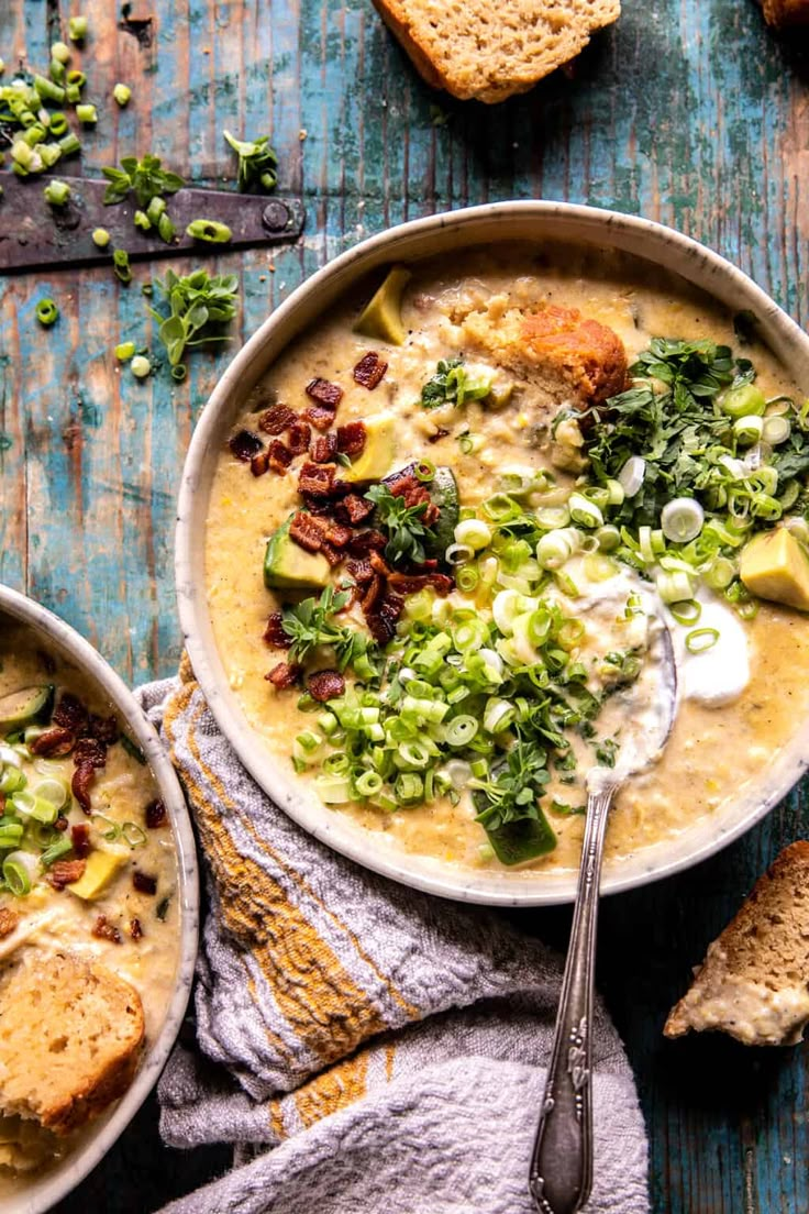 two bowls of soup with bread and vegetables on the side, one bowl is full of soup